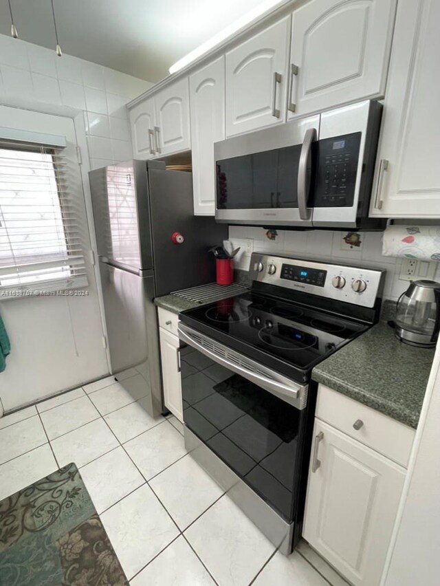 kitchen featuring light tile patterned floors, backsplash, white cabinets, and stainless steel appliances