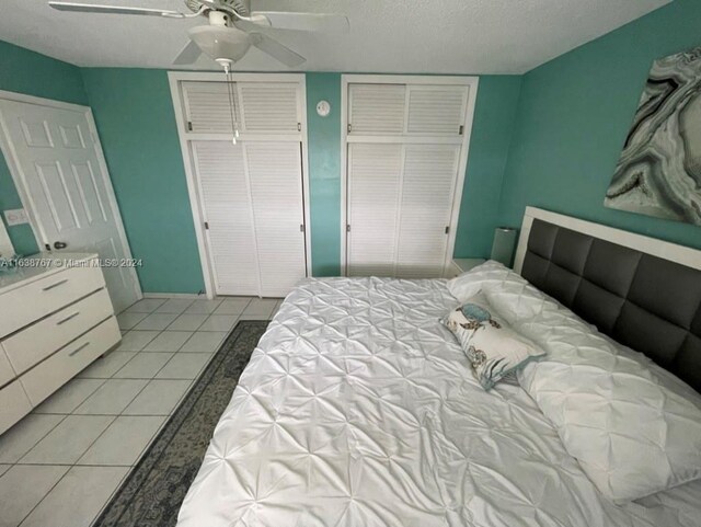 tiled bedroom with two closets, ceiling fan, and a textured ceiling