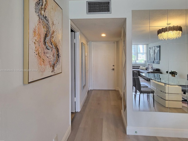 hallway featuring light wood-type flooring, a textured ceiling, and a chandelier