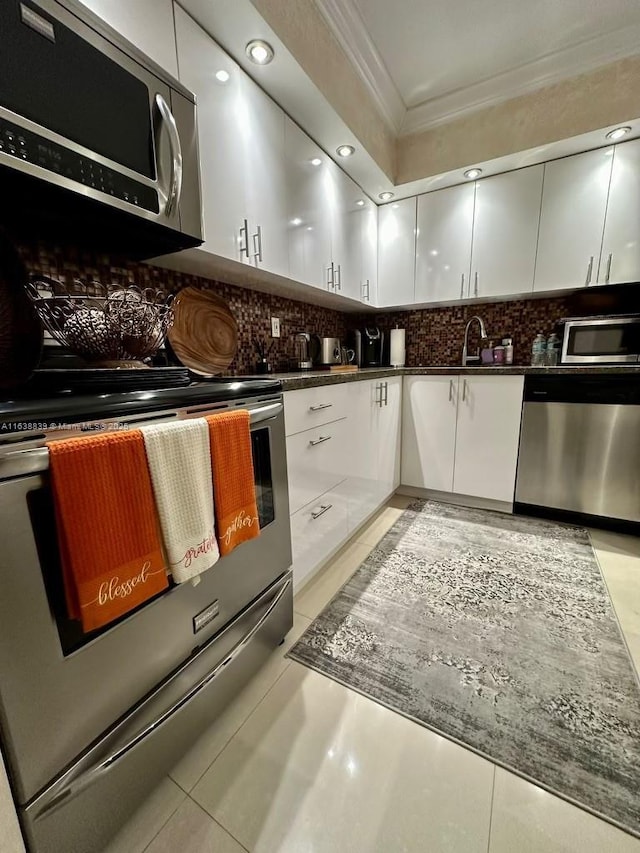 kitchen featuring appliances with stainless steel finishes, backsplash, crown molding, light tile patterned floors, and white cabinets