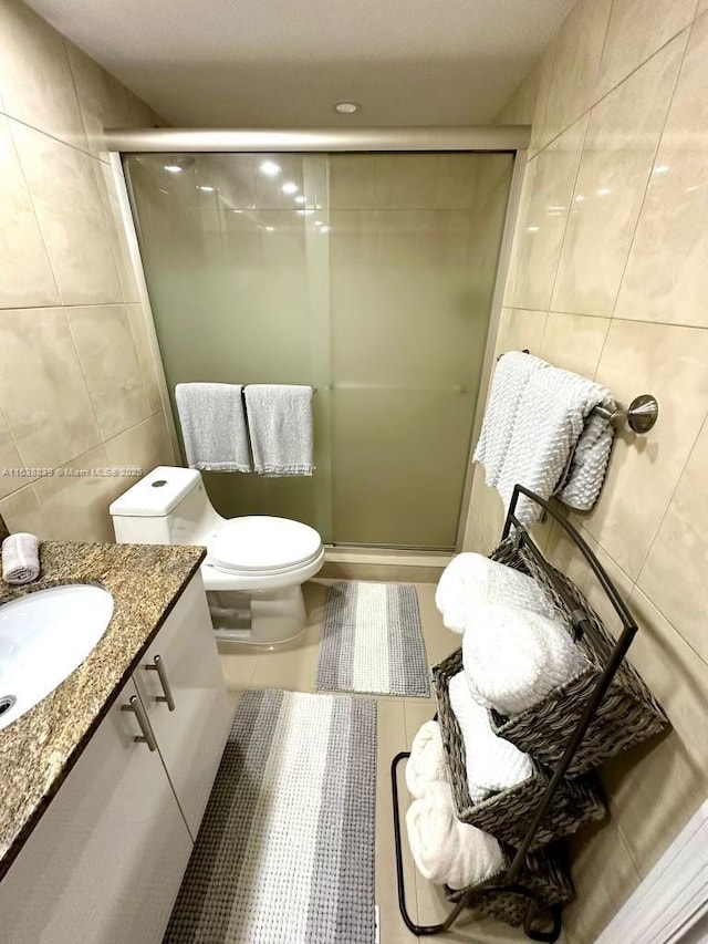 bathroom featuring tile patterned floors, an enclosed shower, toilet, vanity, and tile walls