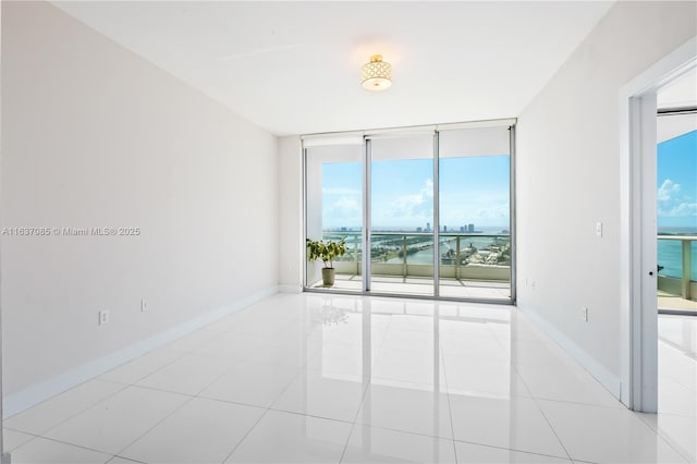 empty room featuring light tile patterned floors, a wall of windows, and a water view