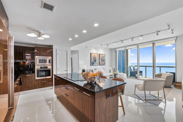 kitchen featuring light tile patterned floors, stainless steel appliances, a center island, a water view, and ceiling fan