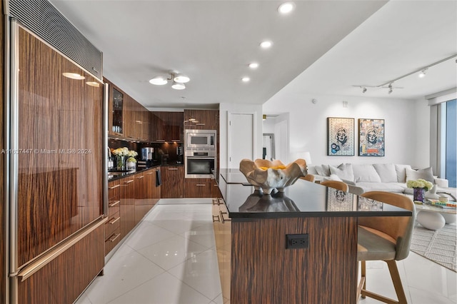 kitchen with built in appliances, light tile patterned floors, a center island, track lighting, and a breakfast bar area