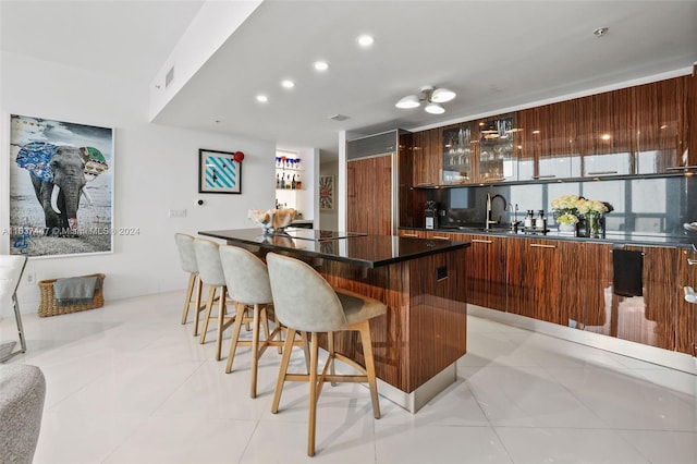 kitchen with a kitchen bar, light tile patterned floors, sink, and a kitchen island