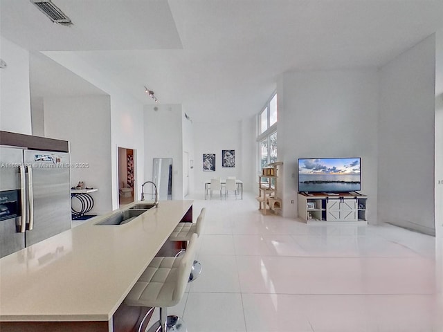 kitchen with sink, a kitchen breakfast bar, a high ceiling, light tile patterned floors, and stainless steel fridge with ice dispenser