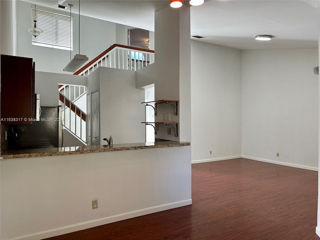 kitchen featuring dark hardwood / wood-style floors, black fridge, kitchen peninsula, a high ceiling, and stone countertops