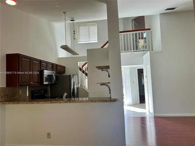 kitchen with appliances with stainless steel finishes, tasteful backsplash, pendant lighting, a high ceiling, and hardwood / wood-style flooring