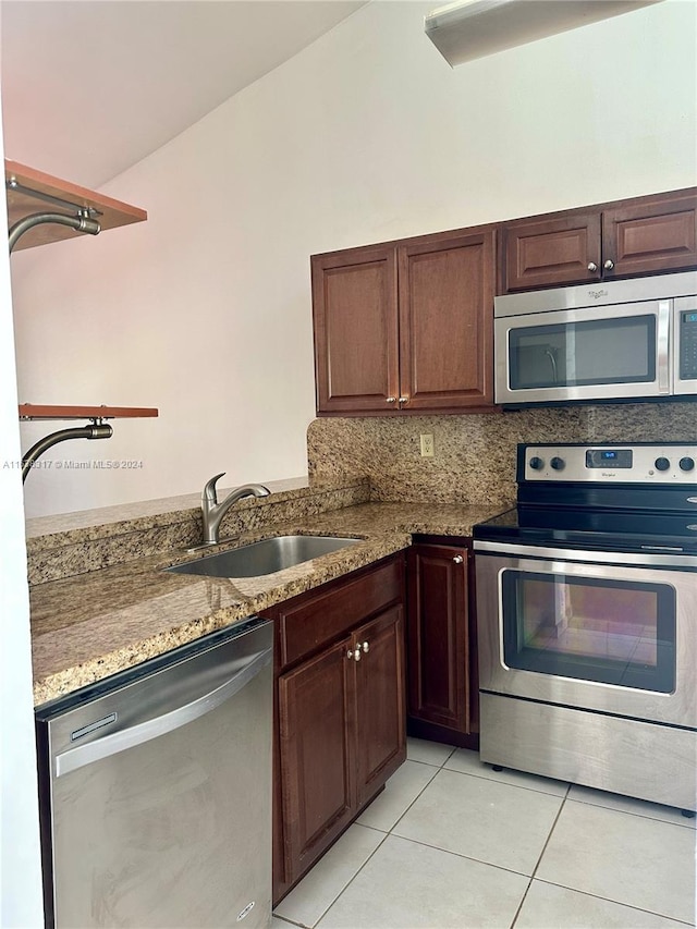 kitchen featuring appliances with stainless steel finishes, vaulted ceiling, backsplash, light tile patterned floors, and sink