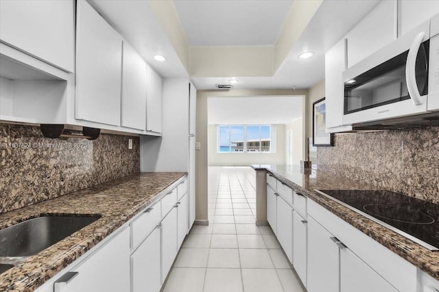 kitchen with black electric stovetop, backsplash, white cabinets, and light tile patterned flooring