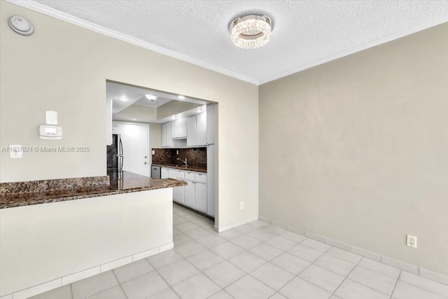 kitchen with freestanding refrigerator, ornamental molding, a sink, white cabinetry, and tasteful backsplash