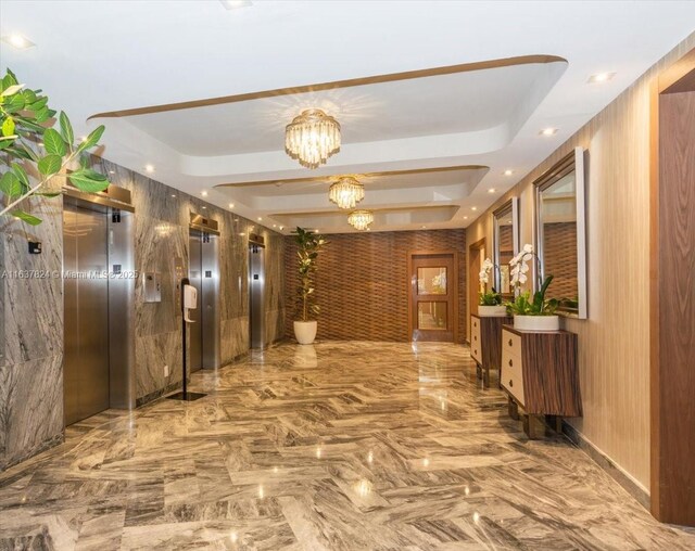 hall with an inviting chandelier, elevator, and a raised ceiling