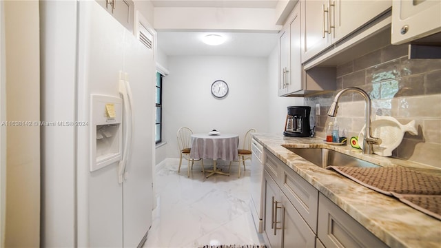 kitchen with decorative backsplash, light stone counters, white refrigerator with ice dispenser, light tile patterned floors, and sink