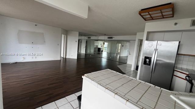 kitchen with light wood-type flooring, stainless steel refrigerator with ice dispenser, and tile counters