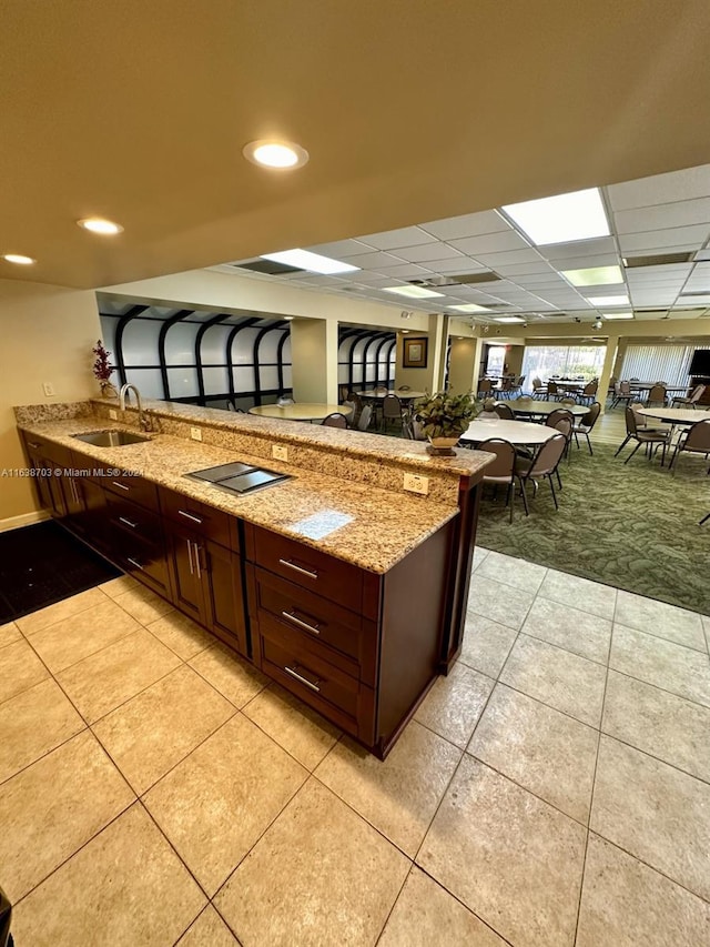 kitchen with sink, light stone countertops, light tile patterned floors, black electric cooktop, and kitchen peninsula