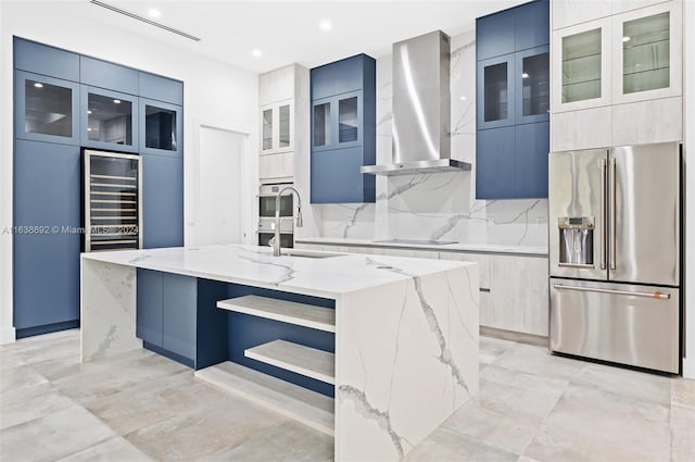 kitchen featuring decorative backsplash, light stone counters, appliances with stainless steel finishes, wall chimney range hood, and a center island with sink