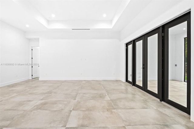 tiled empty room featuring french doors and a tray ceiling