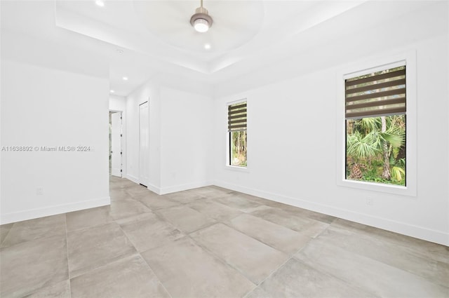 empty room with ceiling fan, a tray ceiling, and light tile patterned floors