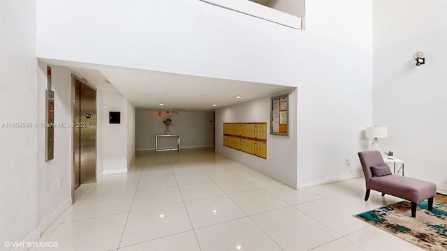 corridor with elevator, light tile patterned flooring, and a high ceiling