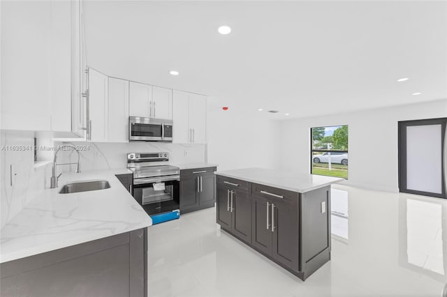 kitchen with light stone counters, a kitchen island, sink, appliances with stainless steel finishes, and white cabinets