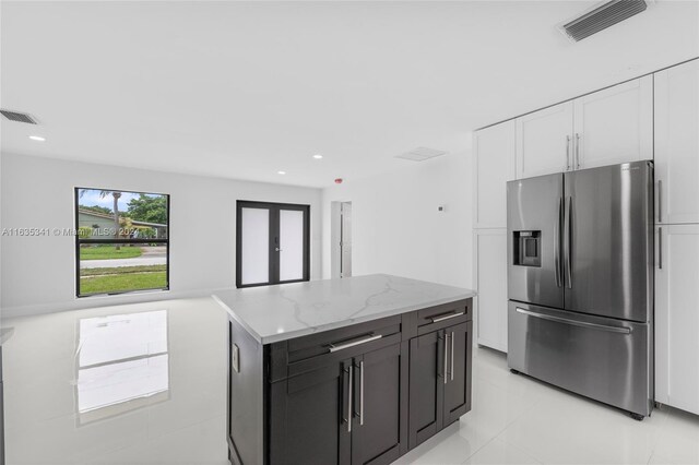 kitchen with a center island, stainless steel fridge, white cabinetry, and light stone countertops