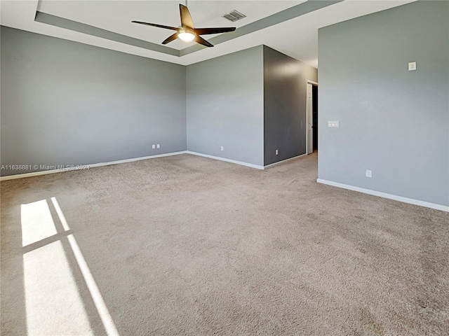 carpeted empty room featuring ceiling fan and a raised ceiling