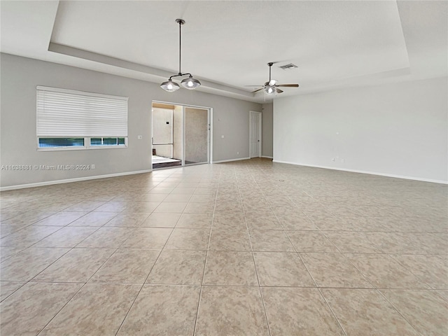 empty room with light tile patterned flooring, ceiling fan, and a raised ceiling