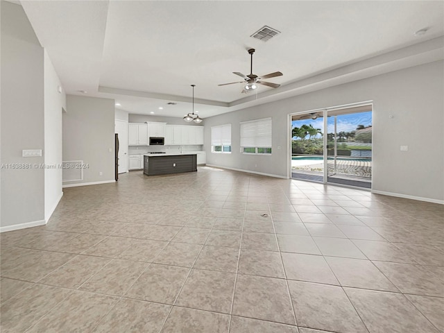 unfurnished living room with light tile patterned floors, ceiling fan, and a raised ceiling