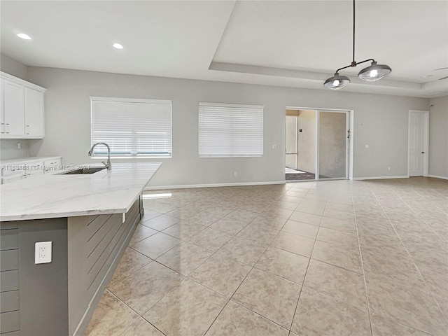 kitchen featuring light tile patterned floors, white cabinets, sink, a raised ceiling, and decorative light fixtures