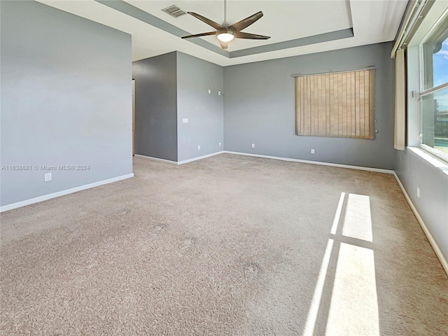 empty room with ceiling fan, a raised ceiling, and carpet floors