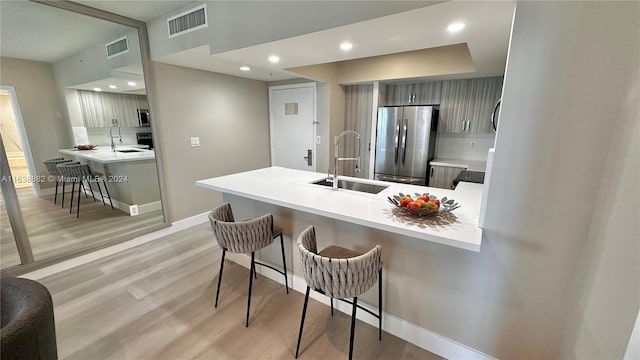 kitchen with sink, a breakfast bar area, light wood-type flooring, kitchen peninsula, and stainless steel appliances