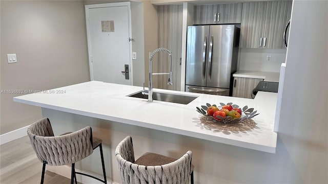 kitchen with sink, a breakfast bar area, stainless steel fridge, kitchen peninsula, and light hardwood / wood-style flooring