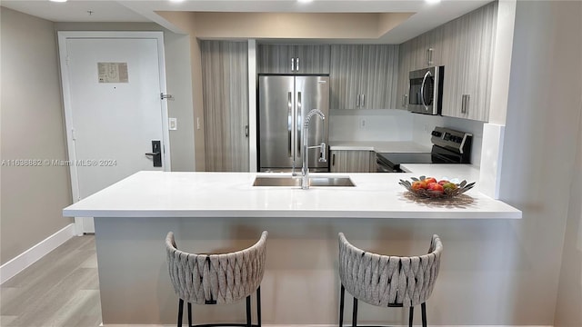 kitchen with gray cabinetry, stainless steel appliances, a kitchen bar, kitchen peninsula, and light wood-type flooring