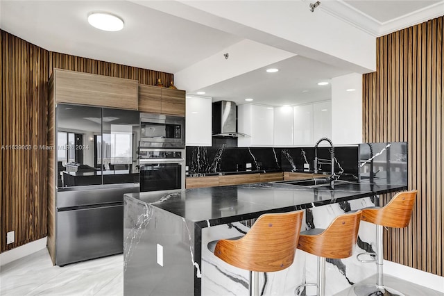 kitchen with wall chimney exhaust hood, a breakfast bar area, built in appliances, backsplash, and sink