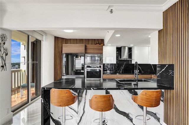 kitchen featuring wall chimney exhaust hood, backsplash, crown molding, a kitchen bar, and appliances with stainless steel finishes