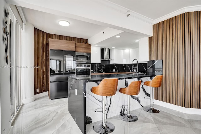 kitchen featuring wall chimney range hood, tasteful backsplash, a breakfast bar area, built in appliances, and sink