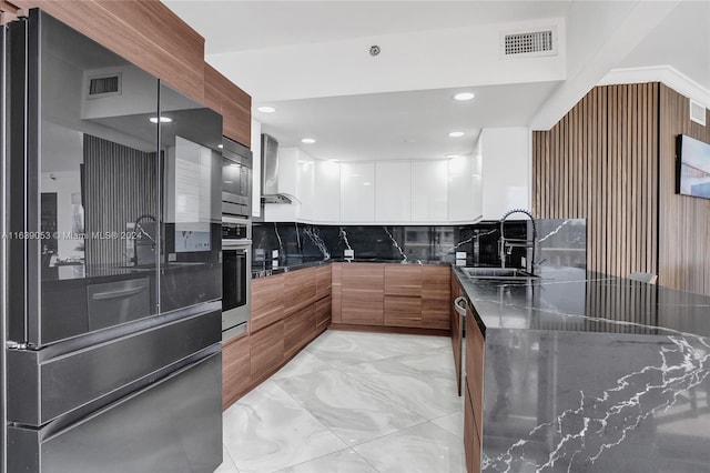 kitchen with appliances with stainless steel finishes, sink, wall chimney exhaust hood, white cabinets, and decorative backsplash