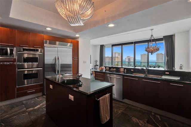 kitchen with a kitchen island, dark stone counters, sink, a chandelier, and appliances with stainless steel finishes