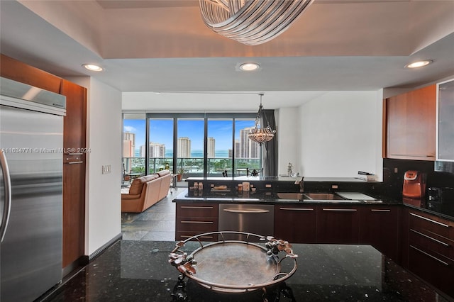 kitchen featuring a chandelier, dark stone countertops, stainless steel appliances, sink, and decorative light fixtures