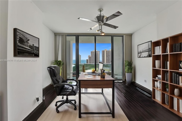 home office with expansive windows, wood-type flooring, and ceiling fan