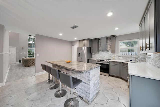 kitchen featuring wall chimney range hood, appliances with stainless steel finishes, gray cabinetry, and a healthy amount of sunlight