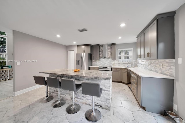 kitchen with gray cabinetry, stainless steel appliances, sink, wall chimney exhaust hood, and a kitchen island