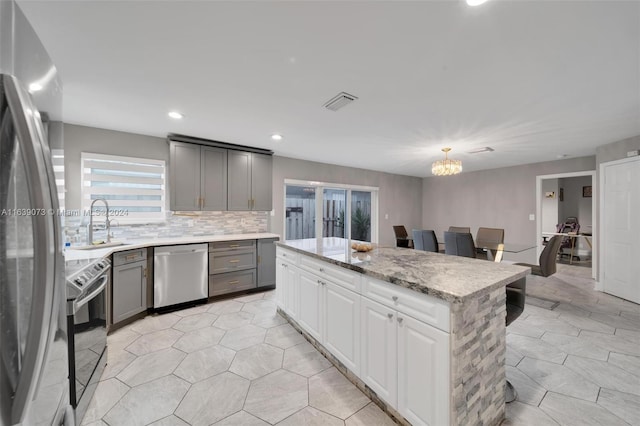 kitchen with gray cabinetry, stainless steel appliances, a notable chandelier, pendant lighting, and a kitchen island