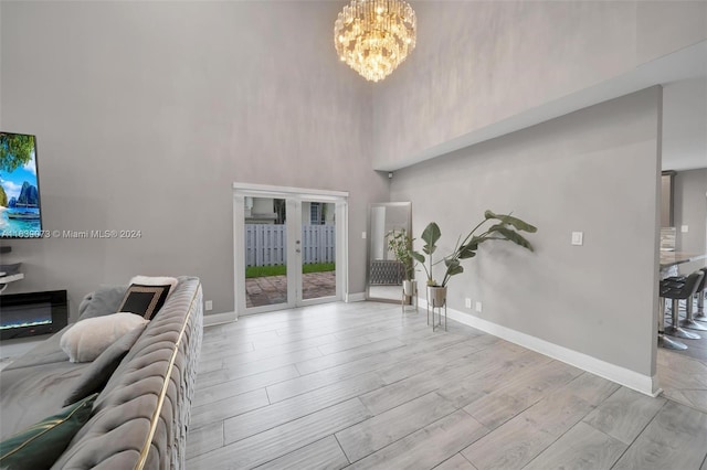 foyer entrance with a high ceiling, a notable chandelier, light wood-type flooring, and french doors