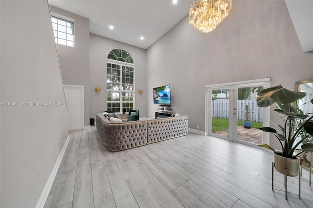 living room with an inviting chandelier, plenty of natural light, light hardwood / wood-style floors, and a towering ceiling