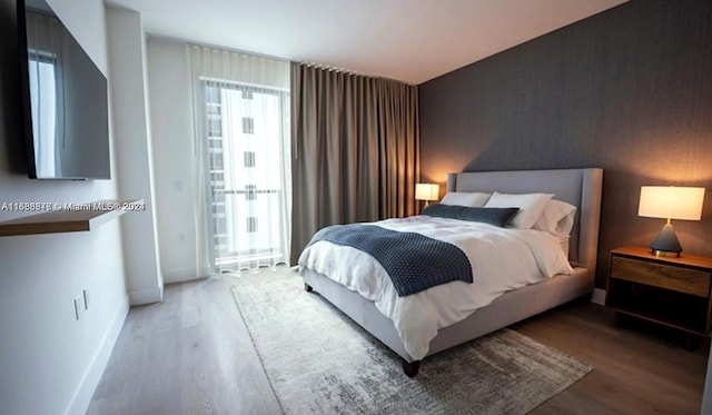 bedroom featuring an accent wall, wood finished floors, and baseboards