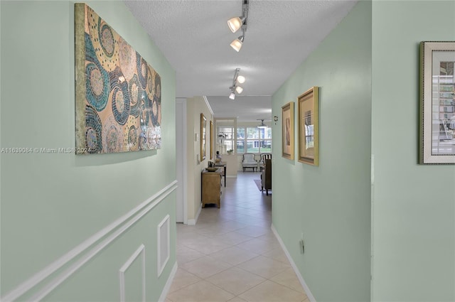 hall featuring a textured ceiling, light tile patterned floors, rail lighting, and baseboards