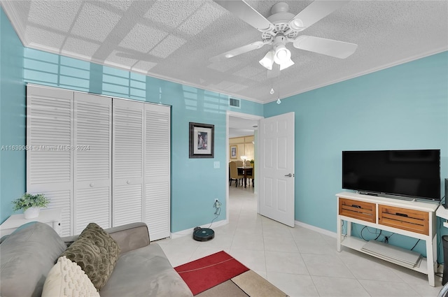 living room featuring ceiling fan, a textured ceiling, ornamental molding, and light tile patterned floors