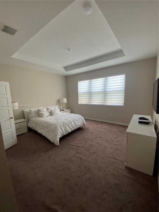 bedroom featuring dark carpet and a tray ceiling