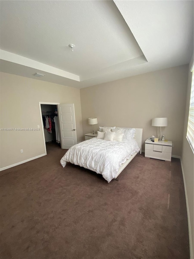 bedroom with dark carpet, a tray ceiling, and a walk in closet